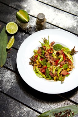 Beyaz bir tabakta Asya yemeği. Kızarmış ördek, mango, avokado ve susam ile Salata