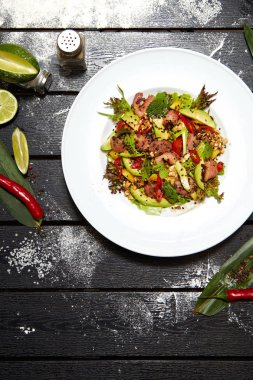 Beyaz bir tabakta Asya yemeği. Kızarmış ördek, mango, avokado ve susam ile Salata