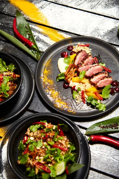 Siyah bir masada Asya yemekleri. Şeftali ile Ördek göğsü, sığır eti ile erişte, tavuk ve karides ile pad tay.