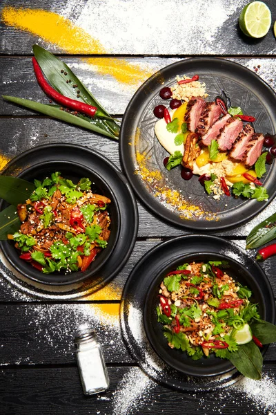 Siyah bir masada Asya yemekleri. Şeftali ile Ördek göğsü, sığır eti ile erişte, tavuk ve karides ile pad tay.