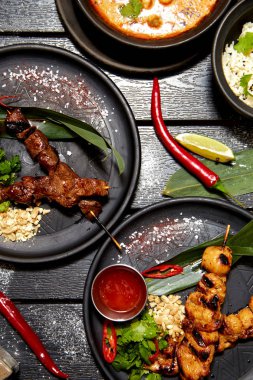 Siyah bir masada Asya yemekleri. Satay ve Tom Yam