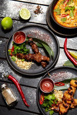 Siyah bir masada Asya yemekleri. Satay ve Tom Yam