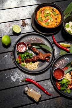 Siyah bir masada Asya yemekleri. Satay ve Tom Yam