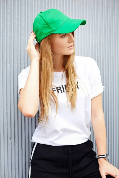 Красивая блондинка в зеленой кепке на фоне серой стены — стоковое фото