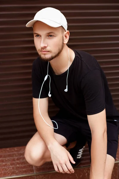 Chico guapo con gorra blanca y camiseta negra con auriculares en la calle —  Fotos de Stock
