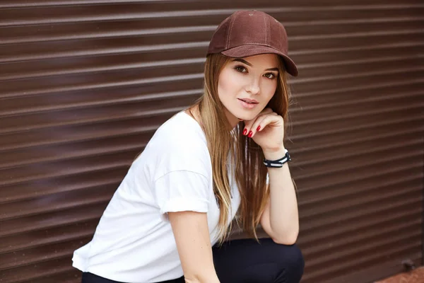 Hermosa chica rubia en una gorra marrón sobre un fondo de pared — Foto de Stock