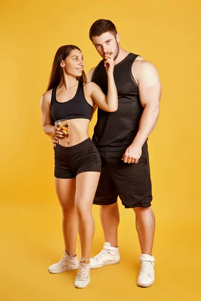 Beautiful couple of athletes with food in studio on a yellow background