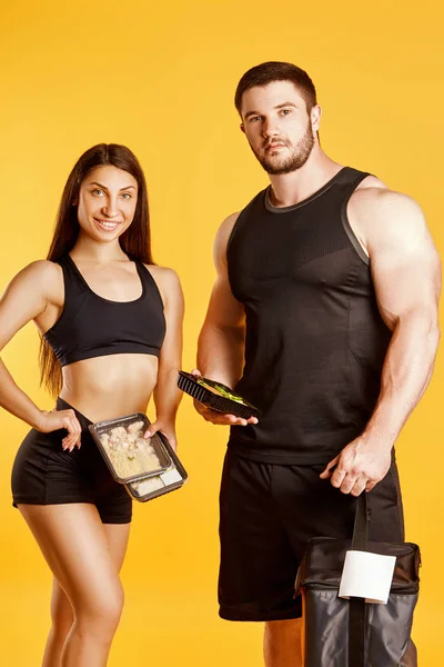 Beautiful couple of athletes with food in studio on a yellow background