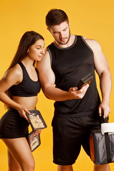 Beautiful couple of athletes with food in studio on a yellow background