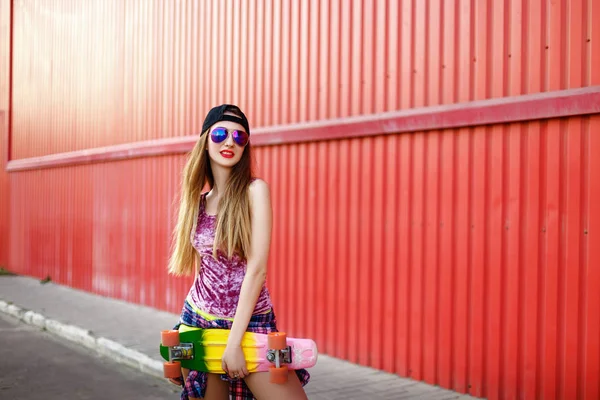 Menina com um skate em um fundo de parede vermelha — Fotografia de Stock