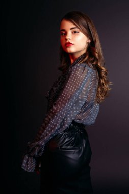 Stüdyoda siyah arka planda bluz ve etek giyen genç bir kız.