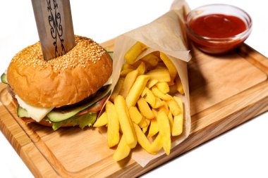 Beyaz arka planda izole edilmiş tahtanın üzerinde patates kızartması ve ketçaplı hamburger.