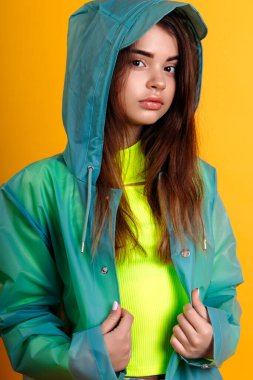 Kot pantolon giymiş genç bir kız ve sarı arka planda stüdyoda yağmurluk.