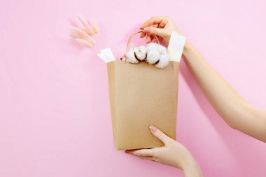 Kadın eli, pembe arka planda çiçekli ve kozmetik ürünlü el çantası.