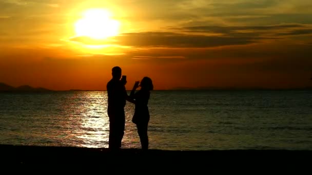 Casal amante tomando selfies enquanto o pôr do sol no mar — Vídeo de Stock