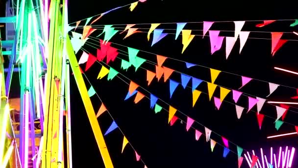 Línea de bandera triangular de colores moviéndose por el viento y la luz de neón ferris rueda — Vídeo de stock