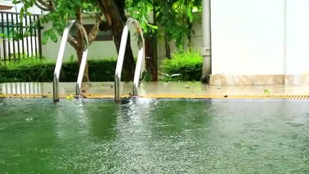 Regen vallen op zwembad wateroppervlak in de buurt van roestvrijstalen trap en groene tuin achtergrond — Stockvideo