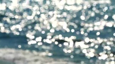 Öğleden sonra su mavisi ve beyaz bokeh yanıp sönme arka planda deniz yüzeyinde dalga bulanık yansıması