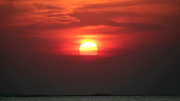 Puesta de sol de nuevo en el cielo oscuro y la nube roja naranja en movimiento pasar el sol sobre el mar — Vídeo de stock