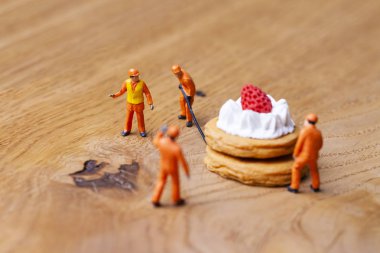 Minyatür insanlar üzerine çilek ile pasta hareket, pişirme ve dekorasyon kavramı. Herhangi bir soruna toplu bir çözüm kavramı. Yakın çekim görünümü. 