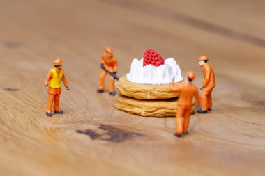 Minyatür insanlar üzerine çilek ile pasta hareket, pişirme ve dekorasyon kavramı. Herhangi bir soruna toplu bir çözüm kavramı. Yakın çekim görünümü. 