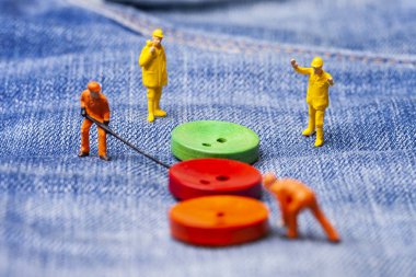 Moda endüstrisi için kavram. Minyatür işçiler için kot düğmeleri büyük iğne dikmek. Yakın çekim.