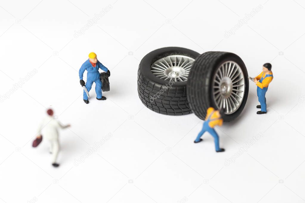 The concept of the workshop tire fitting. Miniature mechanics repairing dusty toy car wheel, close up.
