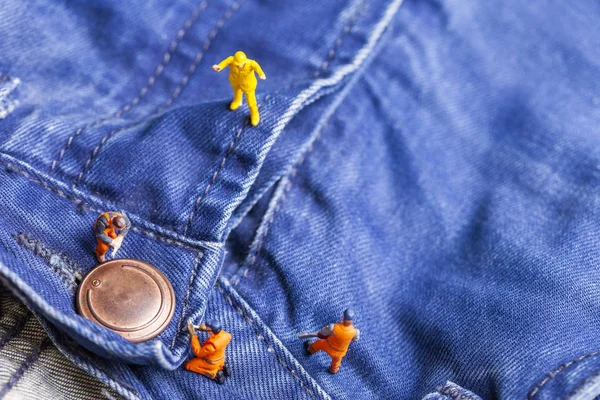 The concept for the fashion industry. Miniature workers on denim texture. Close up.