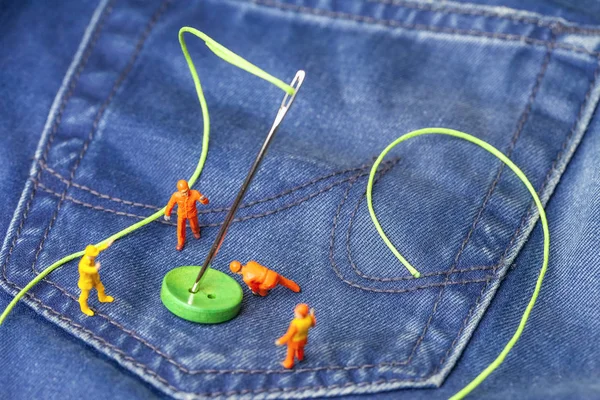 The concept for the fashion industry. Miniature workers on denim texture. Close up.