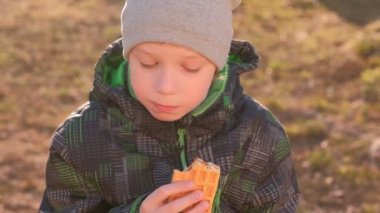 Çocuk parkta bankta oturmuş Waffle yiyor. Önden görünüm.