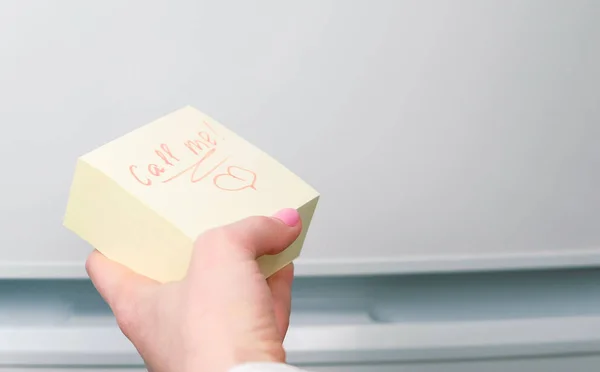 Closeup womans hand writing call me on yellow sticker sheet of paper. — Stock Photo, Image