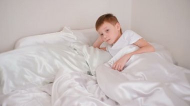 Yedi yaşındaki bir oğlan sessizce odasında yatakta döşeme