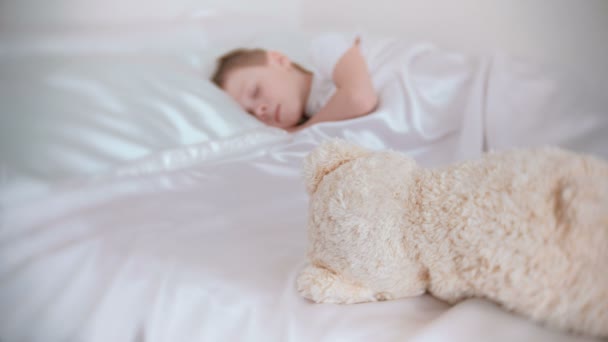 7 歳少年は静かに自分の部屋のベッドで寝て、おもちゃのクマは彼の近きます。ぼかし. — ストック動画