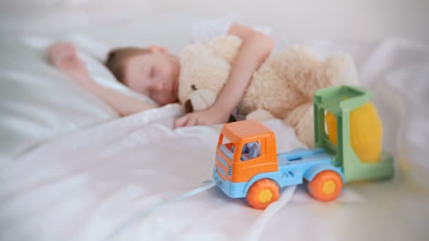Zeven jaar oude jongen met zijn speelgoed Beer en plastic auto slapen. Richten op speelgoedauto. — Stockvideo