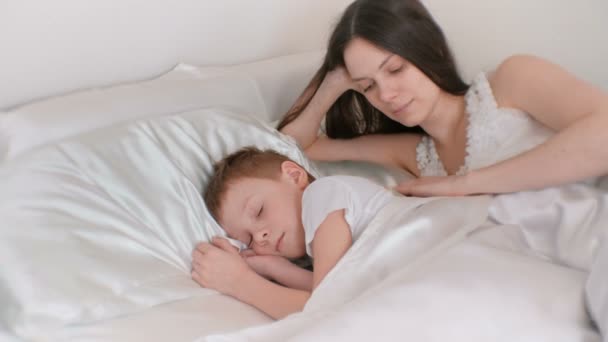 Mutter legt ihren Sohn ins Bett. seinen Rücken streicheln und küssen. — Stockvideo