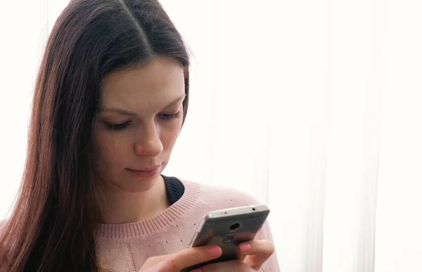 Brunette fiatal nő gépelés egy üzenet-ra-a mozgatható telefon, és nézi a képernyőt. — Stock Fotó