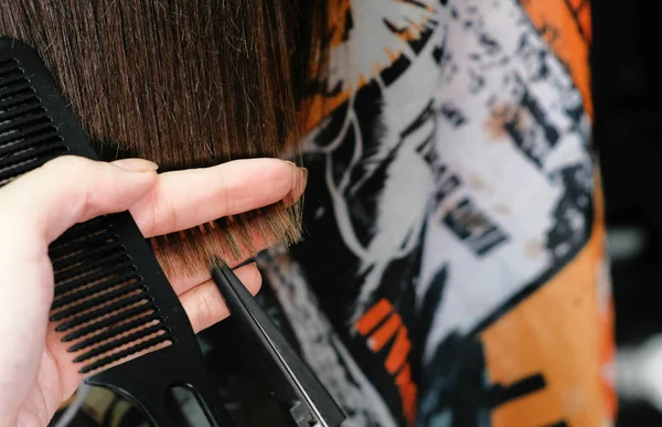 Barbers ruce řezání horkých nůžek dlouhé tmavě hnědé vlasy. Detailní pohled. — Stock fotografie