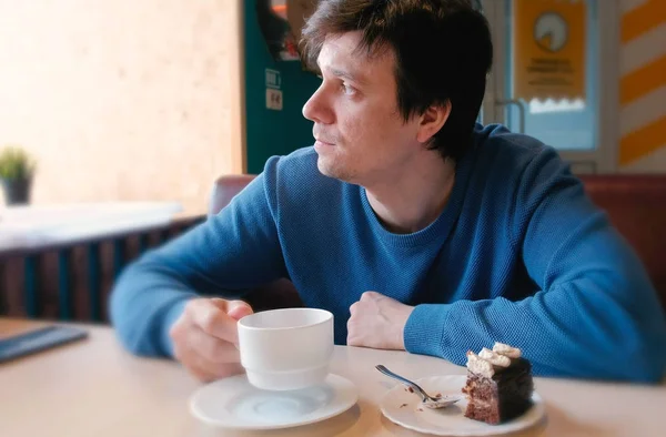 Jonge man kijken venster drinken een kopje thee en eten een fluitje van een cent — Stockfoto