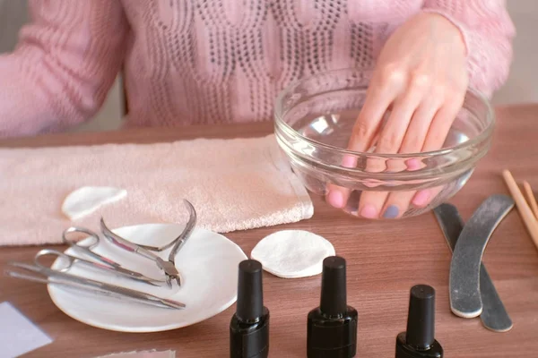 Manicure a casa. Donna che immerge la mano in una ciotola d'acqua. Primo piano a mano, strumenti di manicure sul tavolo . — Foto Stock