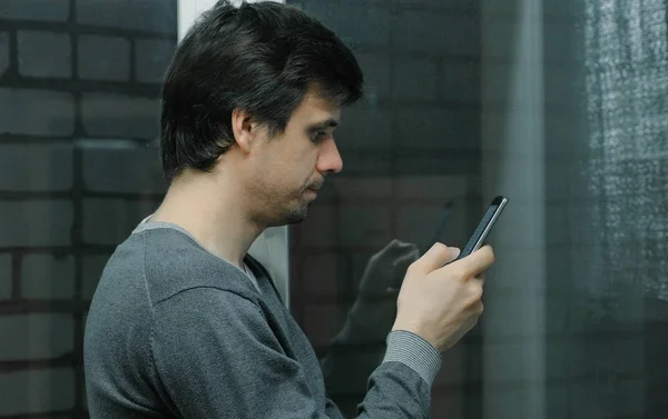 Ember böngészés, internetes oldalak-a mozgatható telefon áll közel az ablakban, az erkélyen. Oldalnézet. — Stock Fotó