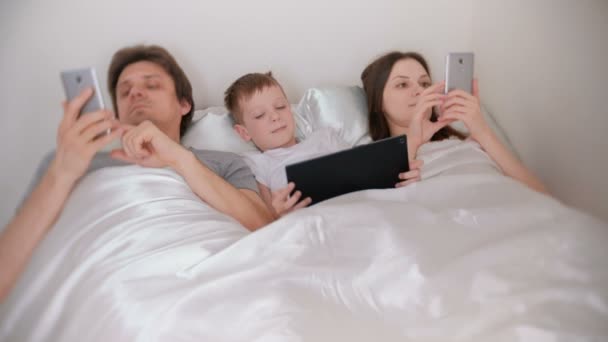 Семья использует мобильные телефоны и планшеты, лежащие в постели утром . — стоковое видео