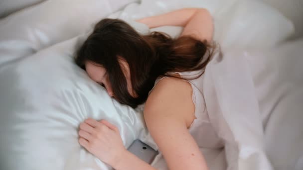 Mujer joven morena durmiendo en la cama. Teléfono móvil cerca de ella . — Vídeos de Stock