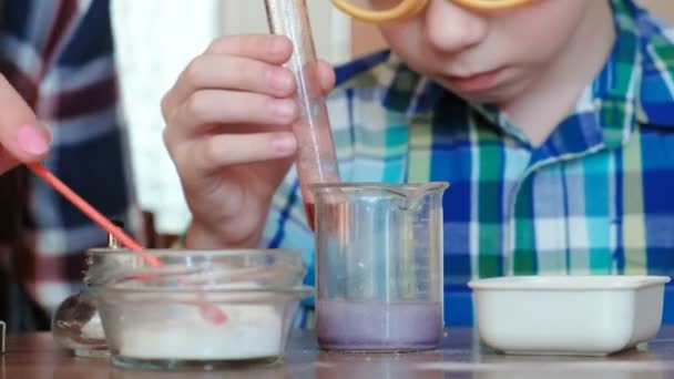 Πειράματα χημείας στο σπίτι. Το αγόρι αγγίζει το υγρό στο δοχείο με το δάχτυλό του. — Αρχείο Βίντεο