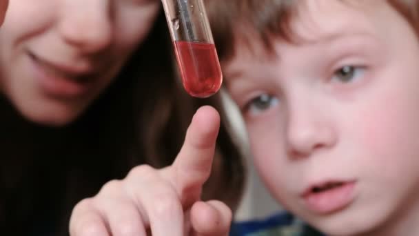 Scheikundige experimenten thuis. Jongen met zijn moeder onderzoekt de rode vloeistof in een reageerbuis. — Stockvideo