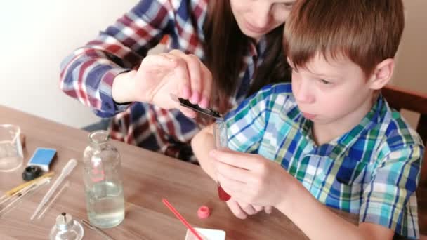 Experimentos de química en casa. Mamá añade una gota de pintura azul al tubo de ensayo con líquido rojo . — Vídeo de stock