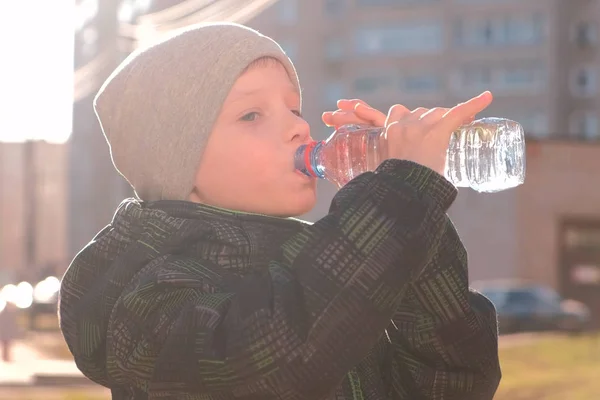 Мальчик пьет воду из бутылки на улице . — стоковое фото