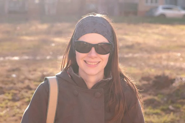 Jovem morena bonita em óculos de sol olha para a câmera e sorri sentado no Parque . — Fotografia de Stock