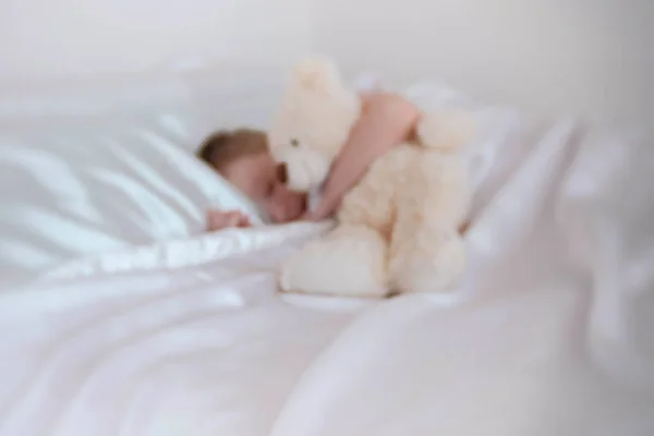 Menino de sete anos acorda abraçando urso de brinquedo. Borrão . — Fotografia de Stock