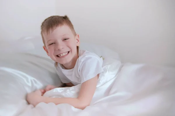 Niño de siete años de edad, acaba de despertar y se ríe mientras está acostado en la cama . — Foto de Stock