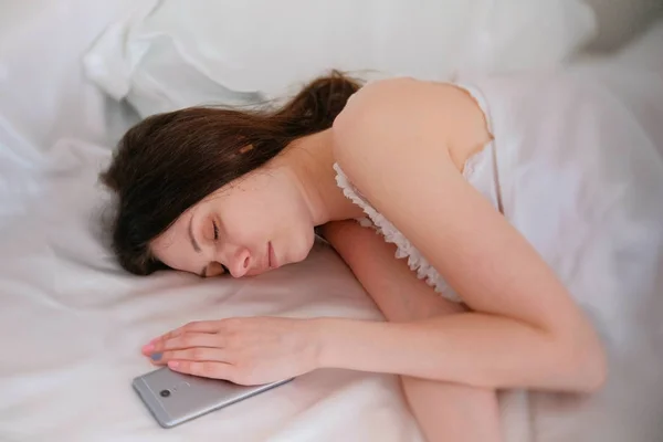 Молодая брюнетка спит в постели. Мобильный телефон рядом с ней . — стоковое фото